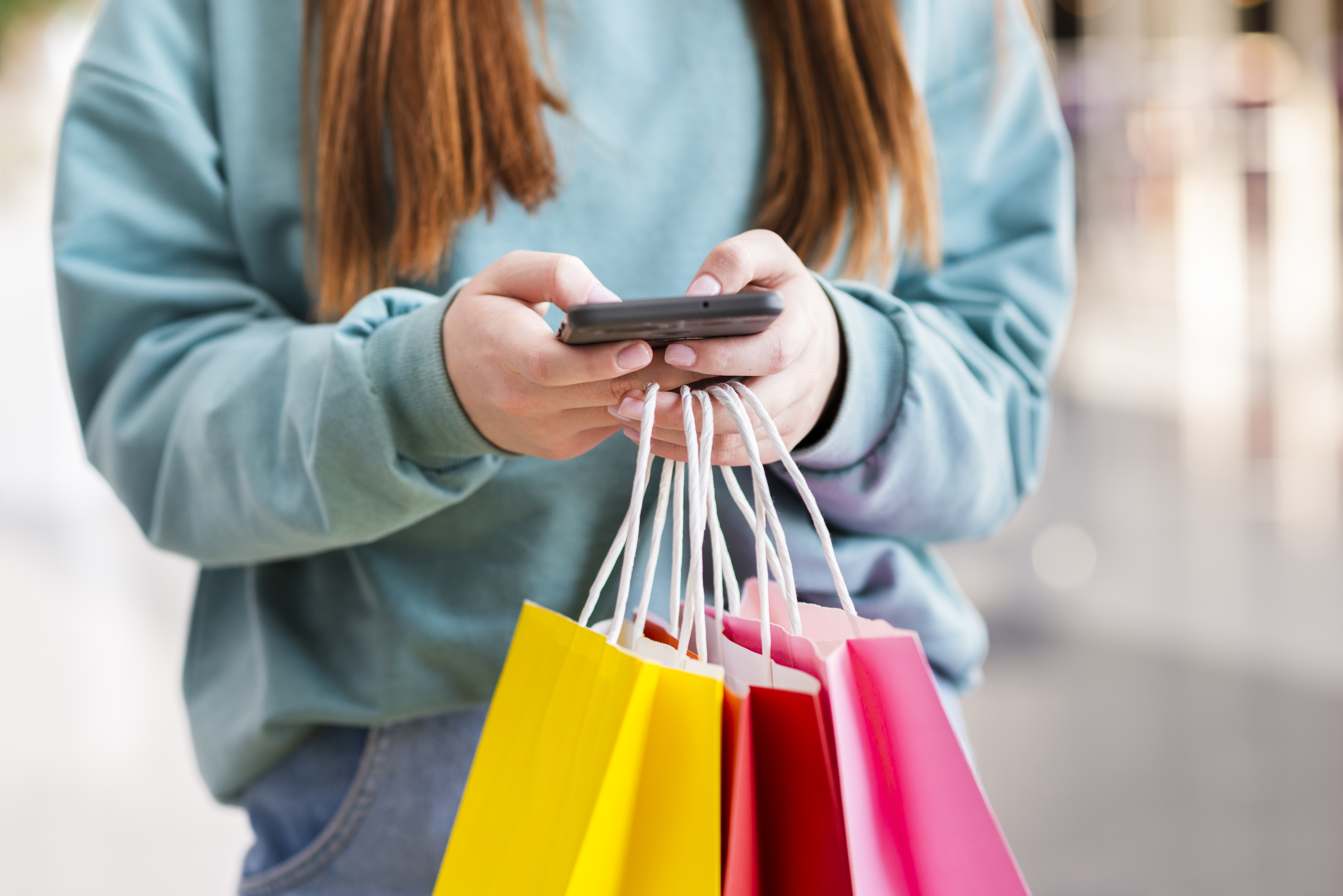 Pessoa segurando sacolas de compras enquanto usa smartphone, representando comportamento do consumidor e ações sazonais