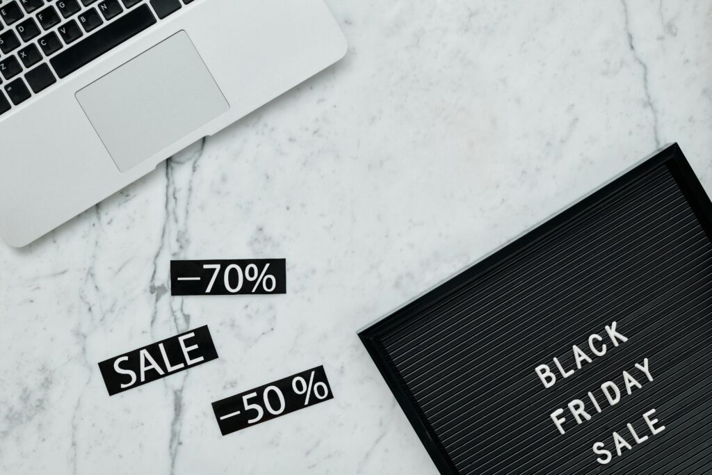 Notebook ao lado de um letreiro escrito "Black Friday Sale" e etiquetas de desconto de 50% e 70%. Representação de estratégias de conversão